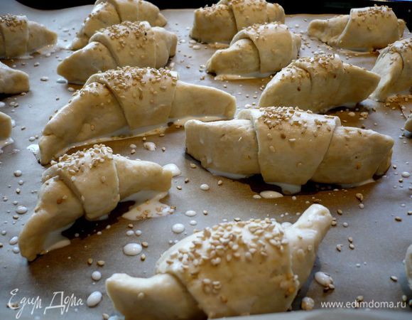 Выложим рогалики на застеленный пекарской бумагой противень. И проделаем то же самое со второй частью теста. Каждый рогалик смажем молоком и обсыпем кунжутом. Поставим в духовку на 25 минут. 