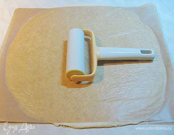 Достать лепешку теста из холодильника, поместить между двух листов пергамента присыпанных мукой и раскатать диаметром 32 см. Очень удобно так раскатывать, во-первых не пачкается рабочая поверхность, во-вторых при раскатывании нужно меньше муки, что позволяет не забить тесто и оно будет крошиться. 