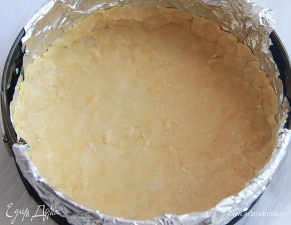 Из ингредиентов для основы приготовить тесто. Раскатать тесто в пласт диаметром на 1см больше формы, в которой будете выпекать пирог. Форму выстелить фольгой или бумагой для выпечки, выложить тесто, прижать ко дну формы, сформировать бортик высотой 1см.