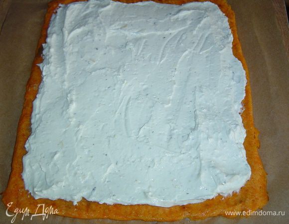 С морковного коржа убираем полотенце, накрываем сверху листом пергамента, переворачиваем на него и аккуратно снимаем нижний лист пергамента.Творожную массу намазываем на морковный корж.