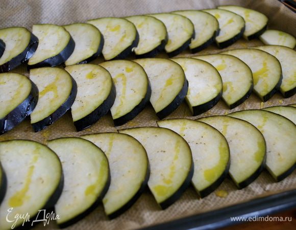 Баклажан нарезать тонкими ломтиками. При желании посолить и оставить на 30 минут, чтобы стек горький сок (я этого не делаю!). Тем временем нагреть духовку до 180 С. Смазать большой противень оливковым маслом, затем слегка смазать дольки баклажанов (2 ст.л.) маслом и уложить их, с некоторым нахлестом на противень. Запекать в духовке в течение 7-10 минут.