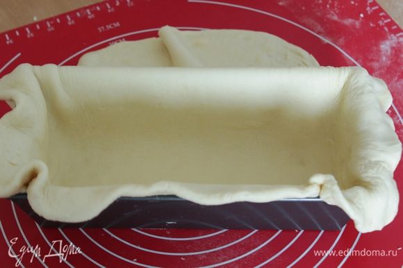 Смазать форму для выпечки. Тесто раскатать в тонкую лепёшку по величине вашей формы так, чтобы уложив в неё тесто, оставались свисать края.