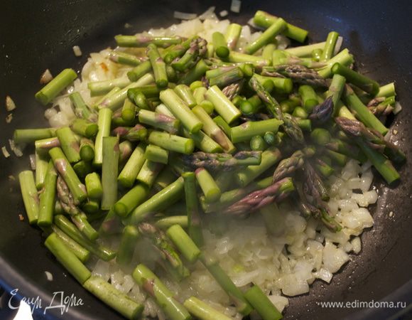В большой сковороде разогреть оливковое масло и положить обжариваться лук и чеснок. Тушить около 5 минут. Затем добавить в сковороду спаржу. Перемешать и обжарить все вместе еще минуты 3.