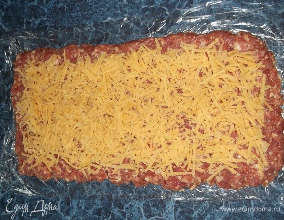 Сверху натереть сыр на крупной терке и выложить поверх фарша, отступая от края 1 см.