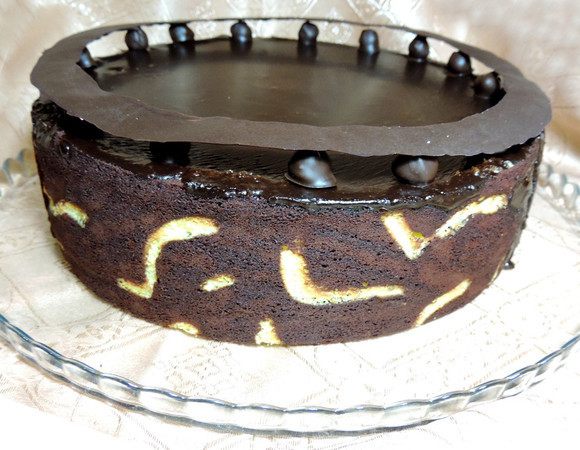  Для украшения нарисуйте на пергаменте растопленным шоколадом обод, больший диаметр которого равен диаметру формы (25 см). Дайте застыть и затвердеть при комнатной температуре. В холодильнике он деформируется! По краю торта в оригинале надо выставить 12 крупных ягодок свежей малины. У меня ее не было и я заменила малину фундуком в шоколаде. Для этого окунула очищенный обжаренный фундук в растопленный шоколад и дала застыть. Сверху на фундук (малину) перед подачей аккуратно устанавливаем шоколадный обод.