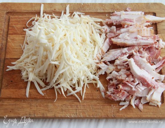 Пока тесто растёт, приготовить начинку. Сыр натереть на крупной тёрке, бекон порезать небольшими полосками.
