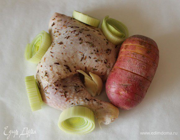 Я заменила репчатый лук на порей. Порей нарезать крупными кольцами, картофель помыть, не чистить... Сделать поперечные надрезы, не дорезая до конца... Дольку чеснока раздавить. Фольгу сложить в два слоя, чтобы получился большой квадрат. На фольгу положить квадрат пергамента такой же величины. Выложить курицу по центру, рядом положить картофель и лук.