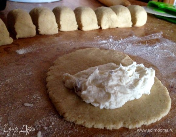 Выложить его на присыпанный мукой стол, аккуратно скатать в цилиндр и разрезать на 10-15 частей. Каждый кусок размять пальцами в лепёшку толщиной 5 мм, положить начинку ближе к верхнему краю.