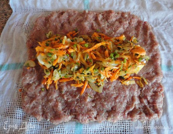 Готовый фарш выложить на мокрую салфетку толщиной в 1 см в виде прямоугольника размером примерно 25  на 25 см.
На середину фарша уложить вдоль сваренные вкрутую  и очищенные целые яйца, предварительно обрезав их с острых концов. Сверху выложить остывший лук с морковью и зелень. 
