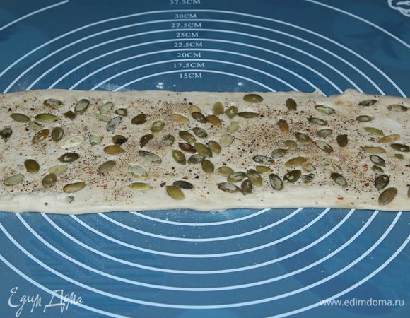 Берем пласт теста, не раскатываем, посыпаем солью, перцем и тыквенными семечками. Слегка прокатываем скалкой, чтобы посыпка приклеилась к поверхности теста. Смазываем растительным маслом.