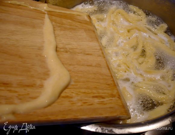Доводим в кастрюле воду до кипения, подсаливаем ее, слегка убавляем огонь, накладываем одну-две столовых ложки теста на увлажненную водой доску, распределяем тесто равномерно по доске и начинаем как бы отщипывать шпателем небольшие кусочки теста и соскабливать их в воду. 