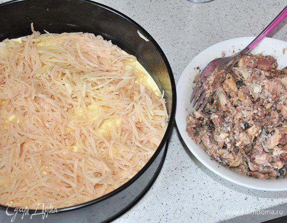 Треть теста вылить в разъемную форму. Выложить потертый на мелкой терке картофель. Сайру растереть вилкой и выложить сверху.