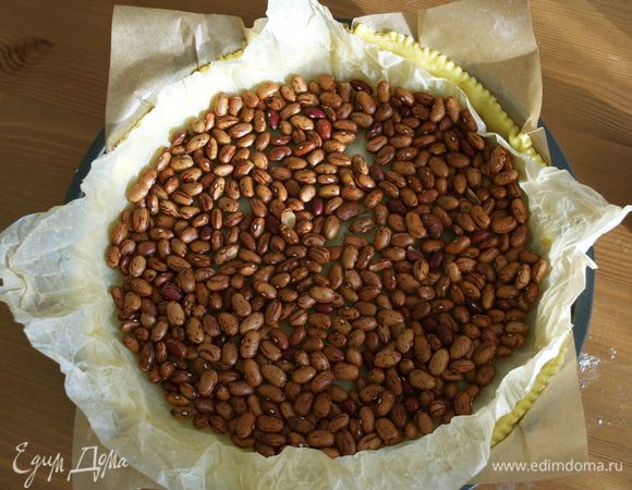 Накрыть тесто листом фольги или пекарской бумаги, сверху насыпать фасоль (или другой "утяжелитель") и поставить форму в разогретую духовку на 20 минут.