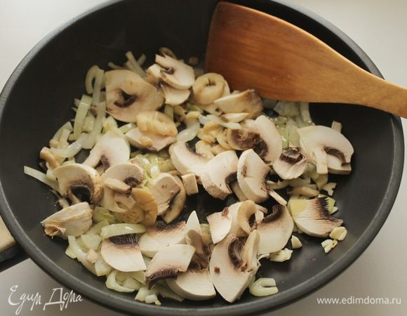 Лук и чеснок очистить и нарезать, обжарить на сковороде в оливковом масле 2-3 минуты,добавить половину грибов.