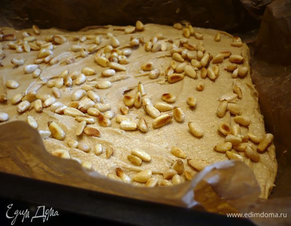 Духовку разогреваем до 180 градусов. Муку смешиваем с разрыхлителем, вводим яйца, творог и начинаем вымешивать, постепенно подливая карамель, до однородности. Прямоугольную форму выкладываем пекарской бумагой. Распределяем тесто, посыпаем орешками.