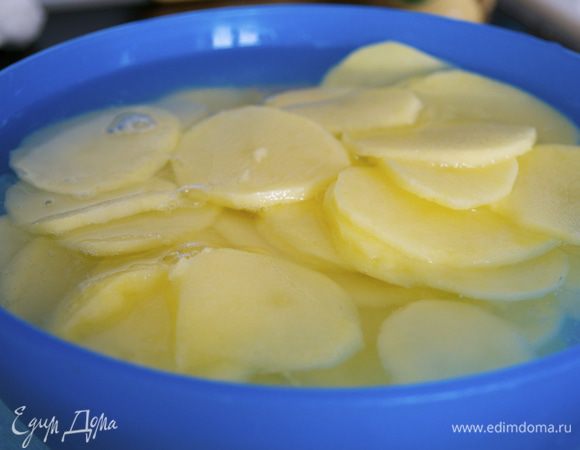 Духовку включить разогреваться на 200 С. Картофель очистить и нарезать тонкими кружочками (лучше всего с помощью овощерезки)... Положить в миску с холодной водой. Измельчить петрушку и укроп.