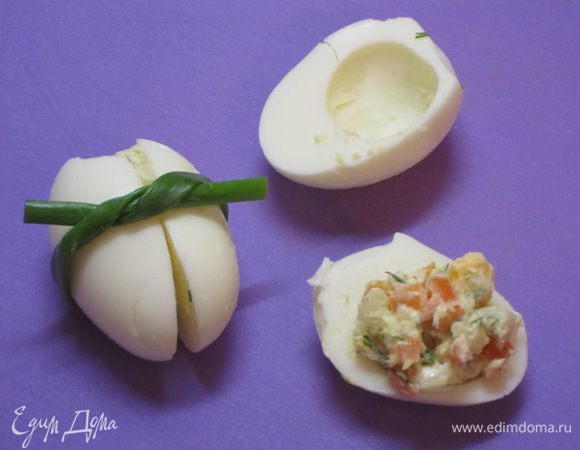 Выложить в 3 половинки белков по 1,5 столовой ложке салата. Накрыть вторыми половинками яиц. Перевязать перьями зеленого лука.