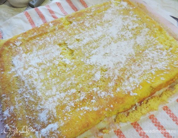 Выпеченный бисквит сразу переворачиваем на чистый лист пергамента. Отделяем пергамент, на котором он выпекался и посыпаем поверхность бисквита сахарной пудрой.