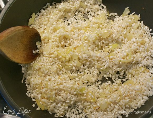 Следите, чтобы лук не зажарился! Как только лук посветлеет, всыпать рис. Перемешать и дать обжариться вместе с луком 1-2 минуты, помешивая.