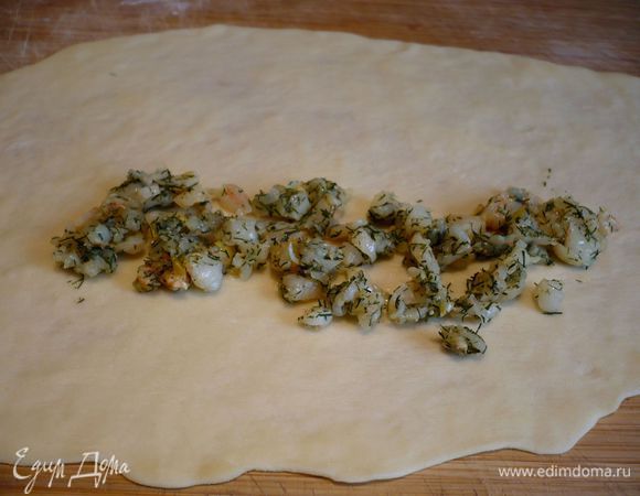 Теперь займемся тестом. Присыпаем поверхность мукой, тесто делим на 4 равные части. Раскатываем каждую часть тонко, а потом тянем его снизу по краям на кулачках, пока оно не станет совсем тонюсеньким. Выкладываем вдоль ближе к краю начинку.