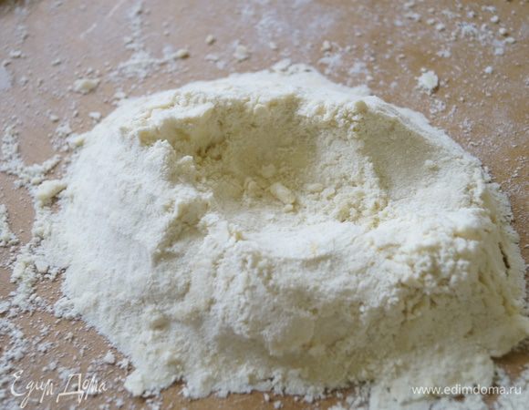 В отдельной чаше смешать муку, соль и сахар. Высыпать на разделочную доску и добавить мягкое, но не растаявшее масло. Перетереть муку и масло между руками в крошку. Сделать з получившейся смеси горку, а в ней углубление.