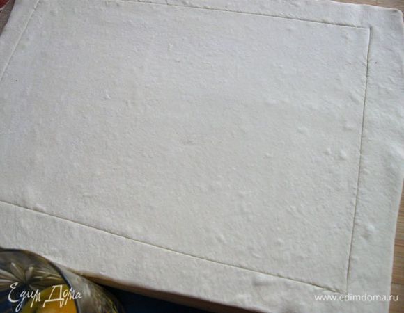 Тесто вынуть из морозильной камеры, разморозить, раскатать по размеру прямоугольной формы  с низкими бортами (у меня форма 24 Х 32),  острым ножом по периметру на расстоянии  2,5 – 3 см сделать разрез не на всю глубину слоя теста, чтобы бортики теста во время выпечки могли подняться. Форму застелить бумагой для выпечки, положить тесто.