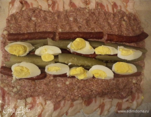 3 яйца отварить, очистить, нарезать четвертушками, также, четвертушками, нарезать сосиски и маринованные огурцы.
На пласт фарша посередине выложить яйца, сосиски и огурцы.
