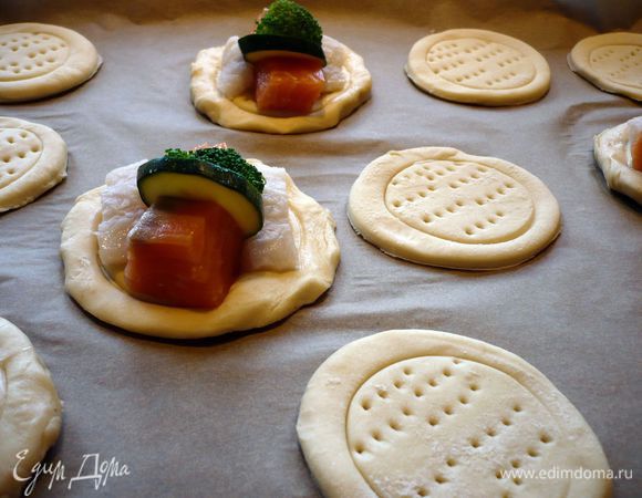 Рыбу снова промокаем полотенцем и солим со всех сторон. Режем рыбу небольшими кубиками. Тесто делим на 2 части. Каждую из которых раскатываем на присыпанной мукой поверхности в пласт. Вырезаем стаканчиком (8 или 9 см диаметром) круги, берем стаканчик поменьше и слегка вдавливаем в круги теста круги поменьше. Накалываем внутренние круги вилочкой. 