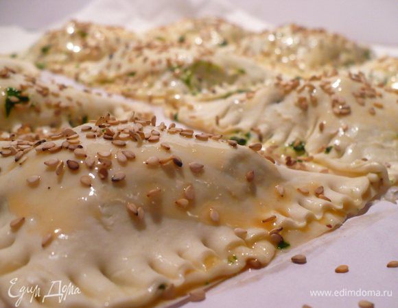 Края обрабатываем желтком. Накрываем вторым концом теста, чтобы получились пышные треугольники. С помощью вилки запечатываем слойки. С помощью кисточки наносим на поверхность слоек желток и посыпаем почти готовые мини-пирожки кунжутными семечками.