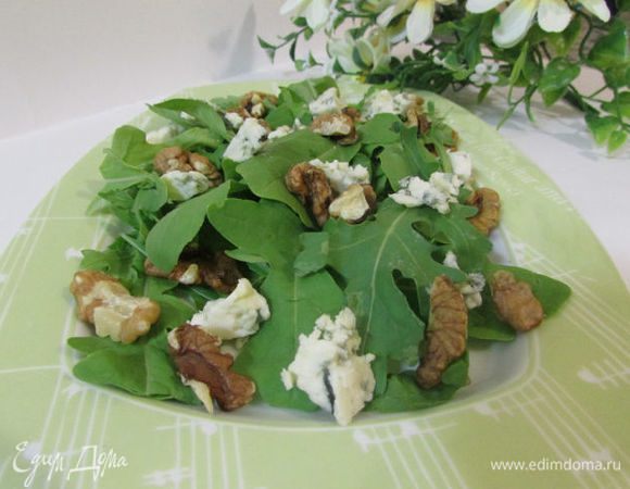 На руколу выложить часть грецких орехов и половину нарезанного мелкими кубиками сыра.