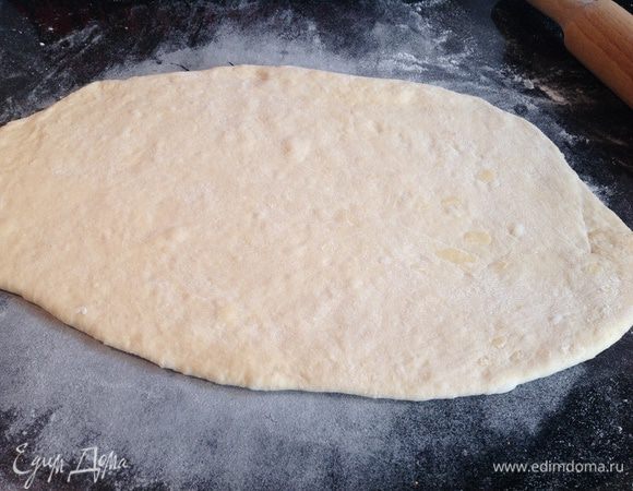 Духовку разогрейте до 180 градусов. Тесто разделите на две части. Раскатайте половину  теста на присыпанной мукой поверхности.