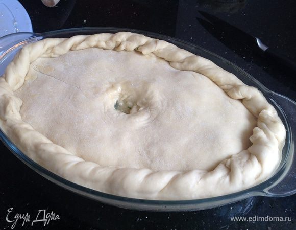 Раскатайте вторую часть тестами накройте ею пирог. Подрежьте края оставив свисать примерно 2 см теста. Расправьте края и красиво загните складками по краю пирога. В центре получившейся крышечки из теста сделайте небольшое отверстие. 