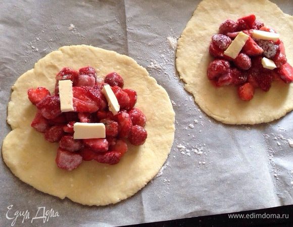 Лепешки перенести на противень застеленный пергаментной бумагой. В центр каждой лепешки выложить клубнику, а сверху по 2-3 небольших кусочка масла.