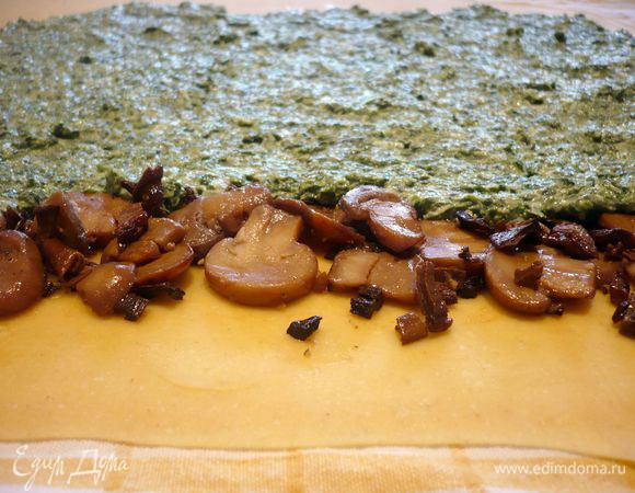 Тесто делим на две части. Одну часть заворачиваем в пленку. Другую раскатываем на припыленной мукой поверхности в тонюсенький пласт в 40 на 30 см. Кладем пласт на полотенце. Отступив примерно 3 см от края выкладываем полоску ½ грибной начинки, разравниваем, оставляя свободные края справа и слева. Следом за грибами распределяем ½ шпинатной начинки. 