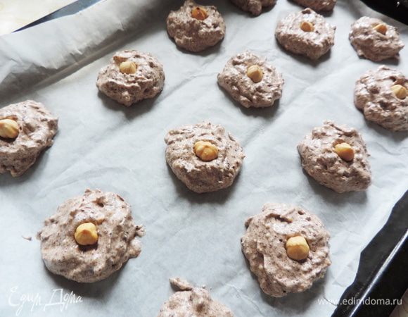 Выкладываем на пергамент печеньки при помощи столовой и чайной ложки. Я брала по столовой ложке без горки теста. Формируем круглые лепешечки. Делайте расстояние между печеньями примерно 1,5 см, так как они немного расплывутся при выпечке. Верх каждой печеньки украшаем фундуком, слегка вдавливая орешек.