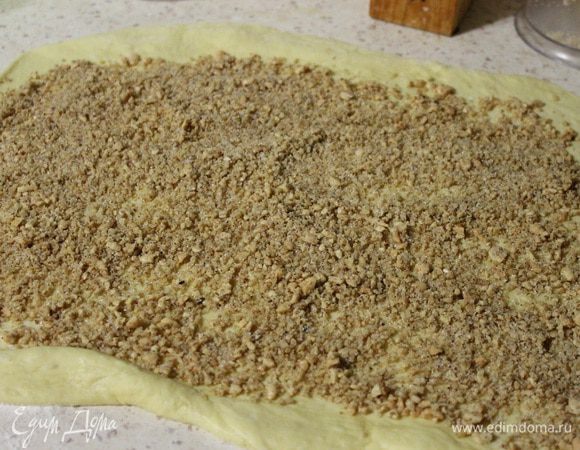 Подошедшее тесто раскатать на припыленном мукой столе, в прямоугольный пласт. Насыпать сверху начинку и разровнять.