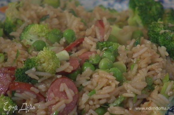 Выложить к рису с колбасками зеленый горошек и обжаривать 2–3 минуты.