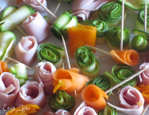 Овощи: цукини нарезать тонкими ломтиками с помощью овощечистки. Свернуть розочкой и скрепить зубочисткой. Из тонко нарезанной ветчины тоже сделать розочки и скрепить зубочисткой. Морковь отварить до полуготовности в кипящей воде, очистить овощечисткой, нарезать тонкими ломтиками, свернуть розочками и скрепить зубочистками. Каждый цветочек подрезать, чтобы они были одинаковой высоты. 
