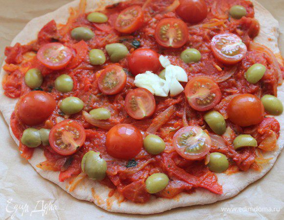 В центр каждой лепешки положить по зубчику раздавленного чеснока. Вокруг разложить половинки помидор черри и оливки.