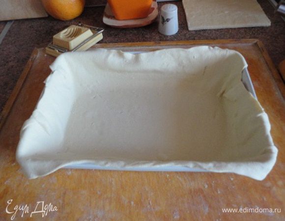 Форму для запекания (у меня примерно 15 на 25 см) смазать сливочным маслом и выстлать тонко раскатанным пластом слоеного теста