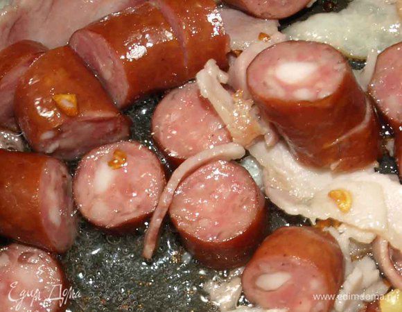 Разогреваем масло в глубоком сотейнике. Охотничьи колбаски режем кусочками, бекон тонкими небольшими полосками, чеснок очищаем и мелко рубим — отправляем в сотейник и обжариваем.