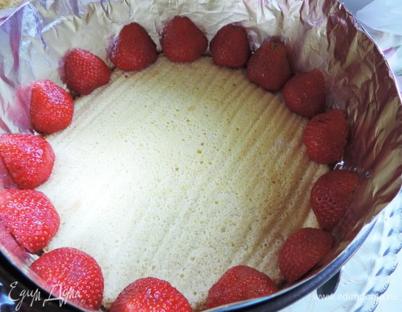 На блюдо выкладываем один бисквитный корж. В оригинале его пропитывали сиропом (вода+сахар+клубничный ликер), но бисквит у меня получился настолько нежным и воздушным, что я его решила не пропитывать. Теперь нам понадобится кондитерское кольцо или бортик от разъемной формы, в которой выпекался бисквит. Его желательно проложить ацетатной пленкой. Она к меня есть, где-то... В общем, ее я не нашла и выстелила боковины кольца фольгой в три слоя. Несколько самых красивых и крупных ягод клубники разрезаем напополам и выкладываем срезом к фольге, оставляя между ягодами промежутки примерно 0,5см.