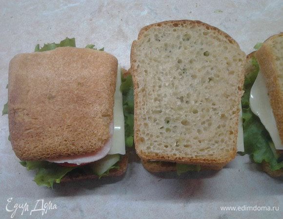Оставшиеся два куска хлеба тоже смазать зеленым маслом с одной стороны и накрыть сандвич. Обматать сандвичи пищевой пленкой и положить под груз минут на 15. Развернуть сандвичи и разрезать по диагонали. Угощайтесь, приятного аппетита.