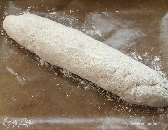 Выложить тесто с помощью скребка на присыпанный мукой стол, сформировать батон (сначала тесто расплющить в прямоугольный пласт, затем свернуть рулетом), уложить на антипригарный лист, накрыть полотенцем и оставить на 1,5 часа до увеличения хлеба в объёме вдвое.
