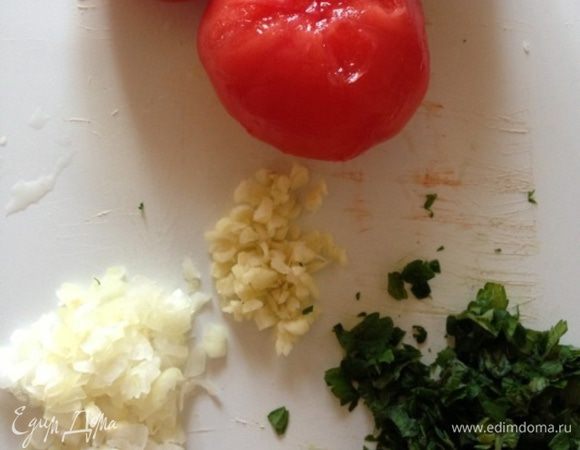 А в это время займемся соусом. Можно использовать готовый, но мы приготовим. Одну небольшую луковицу, чеснок и базилик измельчим. Помидоры надрежем, ошпарим кипятком, снимем с них кожуру и нарежем небольшими кубиками.