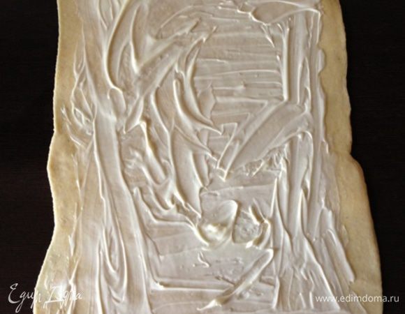 Переместим тесто на сухую рабочую поверхность и раскатаем в прямоугольник. У меня получился приблизительно 25х45 см. Смажем тесто по всей поверхности, отступая по 2 см от краев, размягченным сливочным маслом.