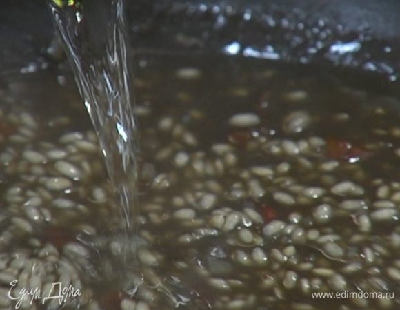 В сковороду с рисом по одному половнику добавлять рыбный бульон, время от времени помешивая ризотто. За 5–7 минут до готовности вынуть чеснок, влить оставшееся вино и все перемешать.