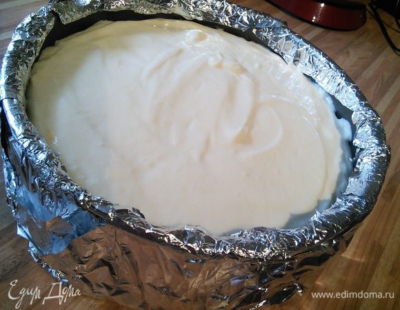 Чизкей будет выпекается на водяной бане, поэтому форму нужно обернуть 2-3 слоями фольги, чтобы вода не попала во время выпечки в форму с чизкейком.
Крем распределите по основе, поверхность разровняйте лопаточкой.
