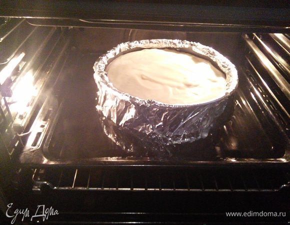 Заранее разогрейте духовку до 175 градусов. Поставьте форму с чизкейком в глубокий противень, в который налейте кипяток. Вода в противне должна доходить примерно до середины формы с чизкейком.
* чизкейк, при выпечке на водяной бане, пропекается равномерно, т.к. пар создаёт более благоприятные условия, чем жар духовки. Выпекайте чиз в течении 1 часа. У готового чизкейка при потряхивании формы середина должна слегка дрожать. При остывании пирог дойдёт до готовности и середина станет упругой. По истечении часа выключите духовку и оставьте чизкейк при приоткрытой дверце 45 мин. отдыхать.