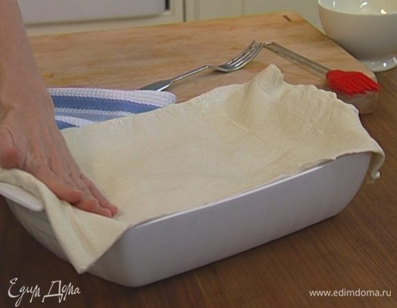Накрыть пластом слоеного теста, слегка прижав его к краям формы.  